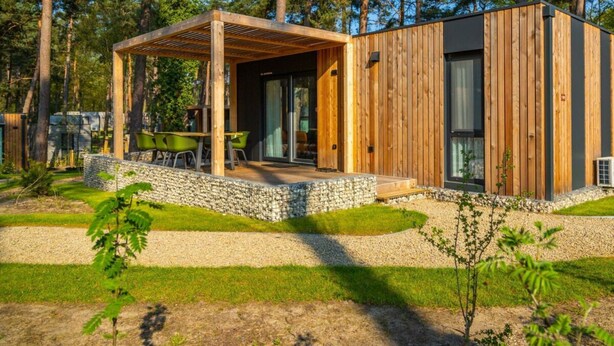 A modern cabin with a wooden exterior, a covered patio with seating, and a stone pathway leading to the entrance. - Lieteberg Cottage 4 (Zutendaal)