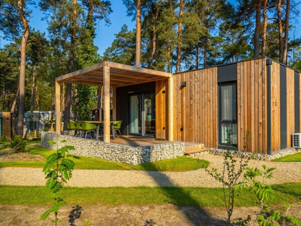 A modern cabin with a wooden exterior, a covered patio with seating, and a stone pathway leading to the entrance. - Lieteberg Cottage 4 (Zutendaal)