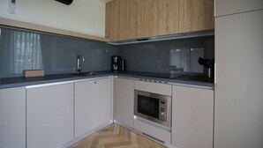 A modern kitchen with wooden cabinets, a built-in microwave, and a coffee maker. - Lieteberg Cottage 4 (Zutendaal)
