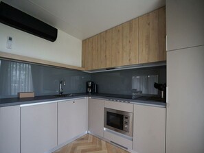 A modern kitchen with wooden cabinets, a built-in microwave, and a coffee maker. - Lieteberg Cottage 4 (Zutendaal)