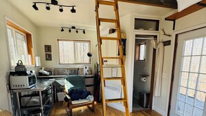 Ein Zimmer mit einer Holzleiter, einem Bett, einer Küchenzeile und einer Tür zum Garten.