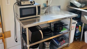 A kitchen with a microwave, kettle, and various utensils on a stainless steel countertop.