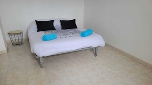 Uma cama com colchão branco, duas almofadas pretas e duas toalhas azuis.