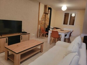 Ein Wohnzimmer mit Fernseher, Holzmöbeln, einer Ziegelwand und einem Essbereich mit Stühlen und einem Tisch.