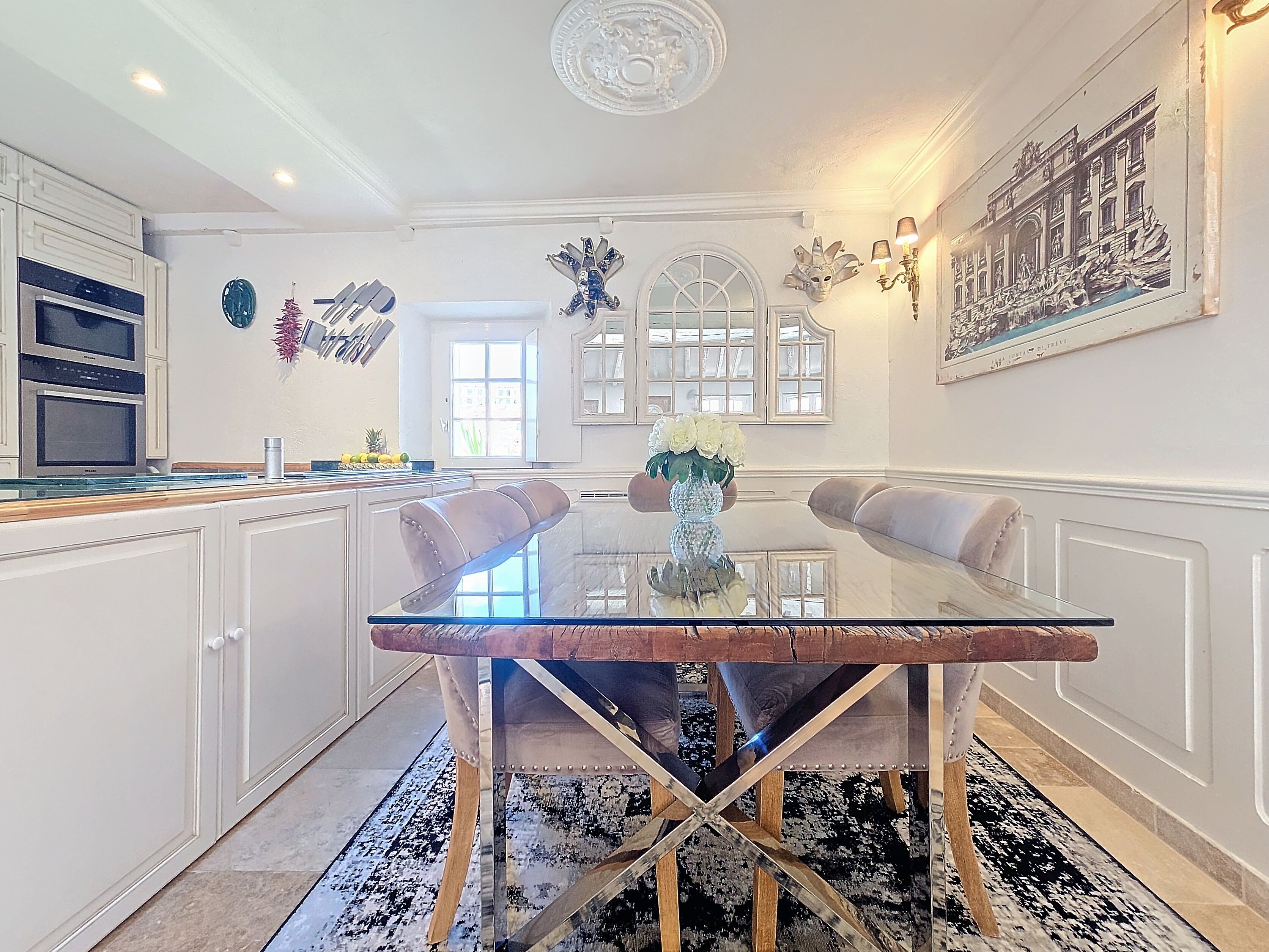 Un coin repas avec une table en verre, des chaises, un vase de fleurs et un tableau au mur.