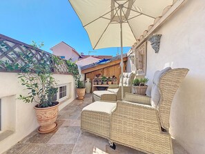Eine Terrasse mit Korbmöbeln, Topfpflanzen und einem großen Sonnenschirm.