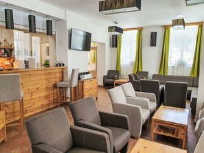 Moderni oleskelutila, jossa on puinen baaritiski, useita erilaisia istumapaikkoja, kuten sohvia ja nojatuoleja, litteänäyttöinen televisio ja puinen sohvapöytä.