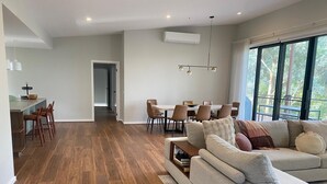 A modern living room with a grey sofa, wooden flooring, and a dining area with chairs and a table. - Escape to Nature in Our Warm & Welcoming Family Home (Warrandyte)