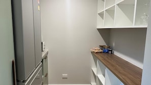 A compact kitchen with a built-in refrigerator, wooden flooring, and white shelving units. - Escape to Nature in Our Warm & Welcoming Family Home (Warrandyte)
