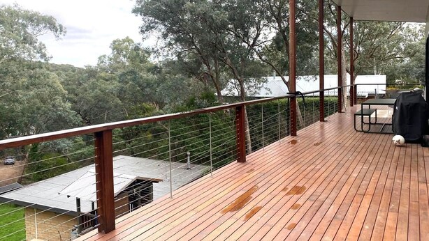 A wooden deck with a metal railing, overlooking a residential area with trees and a white building. - Escape to Nature in Our Warm & Welcoming Family Home (Warrandyte)
