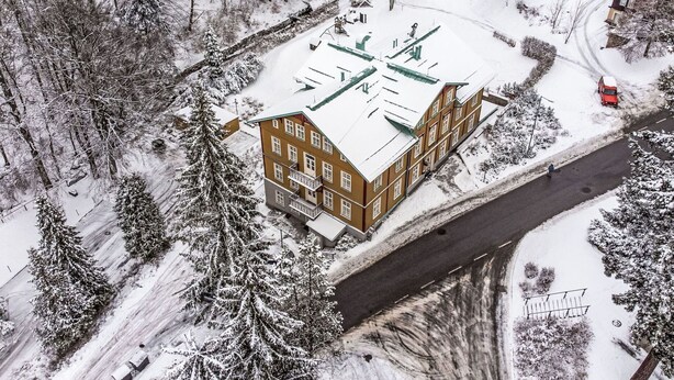 Un edificio de varios pisos con techo plano, rodeado de árboles cubiertos de nieve y una carretera.