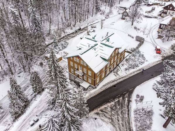 Ein mehrstöckiges Gebäude mit flachem Dach, umgeben von schneebedeckten Bäumen und einer Straße.