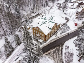 Un immeuble à plusieurs étages, doté d’un toit plat, entouré d’arbres couverts de neige et bordé par une route.