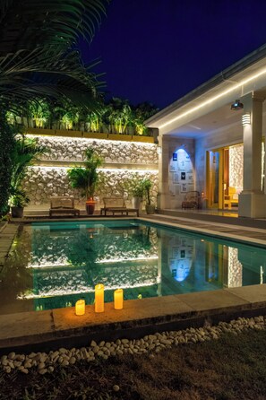 A swimming pool with candles, a stone wall, and lounge chairs. - Villa yellow stone 1 (Kuta utara)