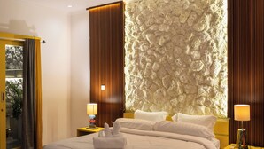 A modern hotel room with a large bed, a stone accent wall, wooden paneling, and a patterned rug. - Villa yellow stone 1 (Kuta utara)