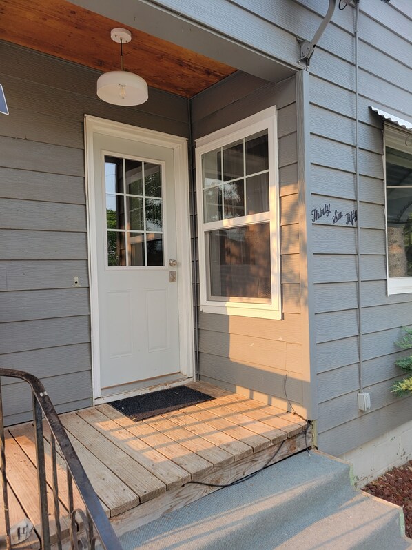 A house with a white front door, a small porch with a wooden railing, and a window with a sign that reads 'Thirty Five.' - Canyon Lake GETAWAY 2 bedrooms-1-KING & 1 QUEEN (Rapid City)