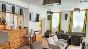 Un moderno salón con barra de madera, diversas opciones de asientos que incluyen sofás y sillones, un televisor de pantalla plana y una mesa de centro de madera.