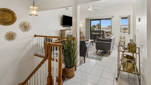 A spacious living area with a staircase, a television, a dining table, and a view through a glass door. - 5 Sea Castles - adorable townhouse with limited ocean view (Fernandina Beach)