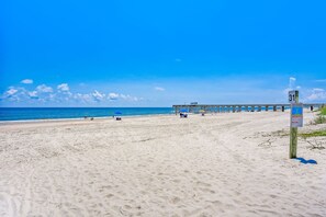 Ein Strand mit einem Steg, der ins Meer führt, ein klarer, blauer Himmel und ein Wegweiser mit der Nummer 31.