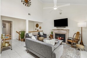 Ein Wohnzimmer mit Sofa, Fernseher, Kamin und Deckenventilator.