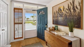 A hallway with a blue door, a wooden bench, a framed artwork, and a view of a green landscape. - 5 Sea Castles - adorable townhouse with limited ocean view (Fernandina Beach)