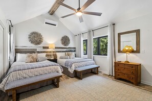 Ein Schlafzimmer mit zwei Betten, einem Deckenventilator, einer Kommode und einem großen Fenster.