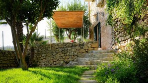 A stone wall, a pathway, and a building with a stone facade and a wooden pergola. - LUES INCANTO (Ragusa)