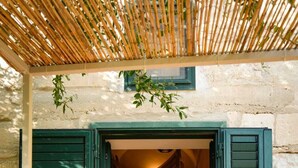 Una puerta con contraventanas verdes, un escalón pequeño que lleva al interior, y un muro de piedra.