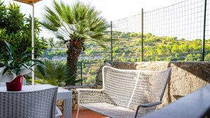Un patio con mobiliario de mimbre, una mesa con una maceta roja y vistas a un paisaje montañoso.