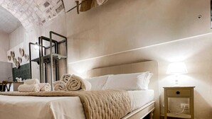 Un dormitorio con una cama, una mesita de noche, un espejo y un perchero para toallas.
