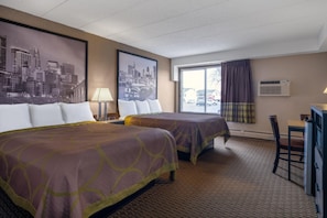 A hotel room with two beds, a desk, a chair, a window with a view of the city, and an air conditioning unit. - Coratel Inn & Suites by Jasper Owatonna (Owatonna)