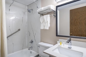 A bathroom with a bathtub, toilet, and sink, marble walls, and a mirror. - Coratel Inn & Suites by Jasper Owatonna (Owatonna)