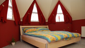 Een slaapkamer met een houten bed, rode gordijnen, een potplant en een radiator.
