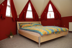 Ein Schlafzimmer mit einem hölzernen Bett, roten Vorhängen, einem Blumentopf und einer Heizung.