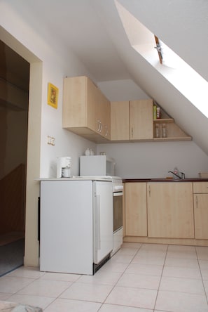 Eine Küche mit weißem Kühlschrank, Mikrowelle und Herd, Holzschränken und einem Oberlicht.