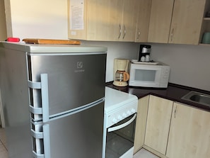 A kitchen with a stainless steel refrigerator, a microwave, a coffee maker, and wooden cabinets.
