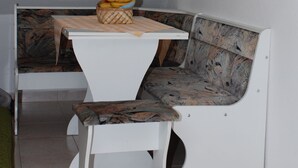 Een zithoek met een tafel en een bank, een mand vol fruit, en een betegelde vloer.