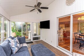 A modern living room with a ceiling fan, a flat-screen TV mounted on the wall, and a sliding glass door leading to a patio area. - Ocean Pines Home with Sunroom and Beach Pass (Ocean Pines)