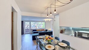 A modern dining area with a glass table, chairs, and a view of the cityscape through large windows. - Lovely apartment for 4 people with WIFI, TV and balcony (Zermatt)