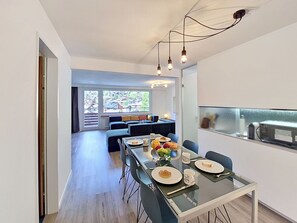 Ein moderner Essbereich mit einem Glastisch, Stühlen und Blick auf die Stadt durch große Fenster.