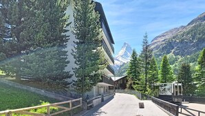 A paved pathway with wooden railings, a mountain backdrop, and a modern building with a sloped roof. - Lovely apartment for 4 people with WIFI, TV and balcony (Zermatt)