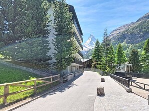 Ein gepflasterter Weg mit hölzernen Geländern, im Hintergrund Berge und ein modernes Gebäude mit geneigtem Dach.