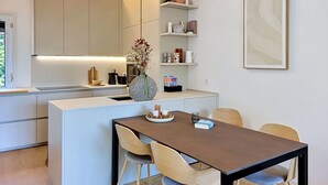 Een moderne keuken met een eethoek, met een centraal kookeiland, inbouwmeubels en een wandplank met decoratieve accessoires.