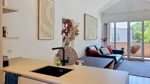 Een moderne keuken met een zwarte spoelbak, een zithoek met een blauwe bank, en een groot raam met uitzicht op de omgeving.