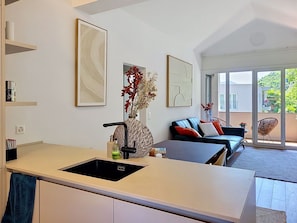 Eine moderne Küche mit einem schwarzen Spülbecken, ein Essbereich mit einem blauen Sofa und ein großes Fenster mit Blick ins Freie.