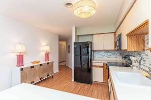 A compact kitchen with a refrigerator, stove, sink, and wooden cabinets. - Bayfront 2BR Condo with Water Views (Ocean City)