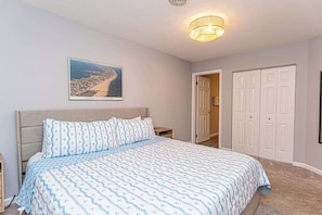 A bedroom with a bed, a nightstand, a wall-mounted picture, and a closet. - Bayfront 2BR Condo with Water Views (Ocean City)