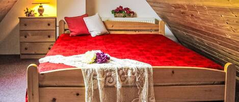 A wooden bed in a room with a sloped ceiling, a nightstand with a lamp, and a framed picture on the wall.