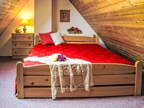 Ein hölzernes Bett in einem Zimmer mit schräger Decke, ein Nachttisch mit Lampe und ein gerahmtes Bild an der Wand.