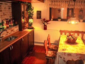 Eine Küche mit Spüle, Holzausstattung, einem Esstisch mit Stühlen, einem Heizkörper und einem Fenster mit Jalousien.